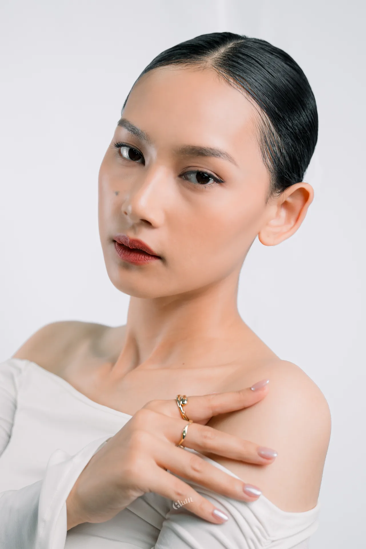 Gina in a white top with gold rings, her hand resting on her collarbone