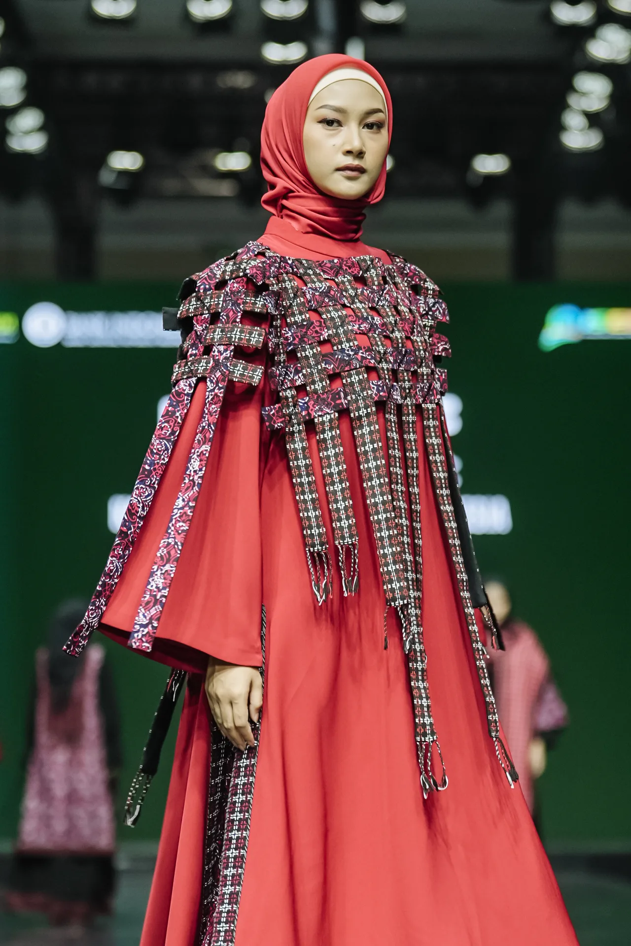 Hijab fashion runway model walking in vibrant red ethnic draped gown with fringed capelet
