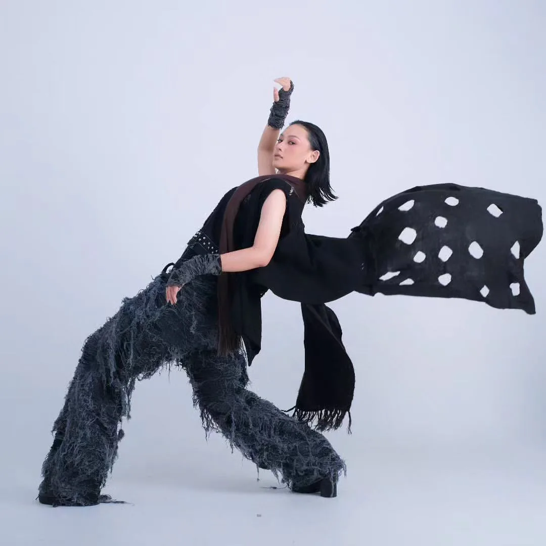 Dynamic high-fashion editorial dance pose of model in shaggy fringe trousers and floating dotted cape